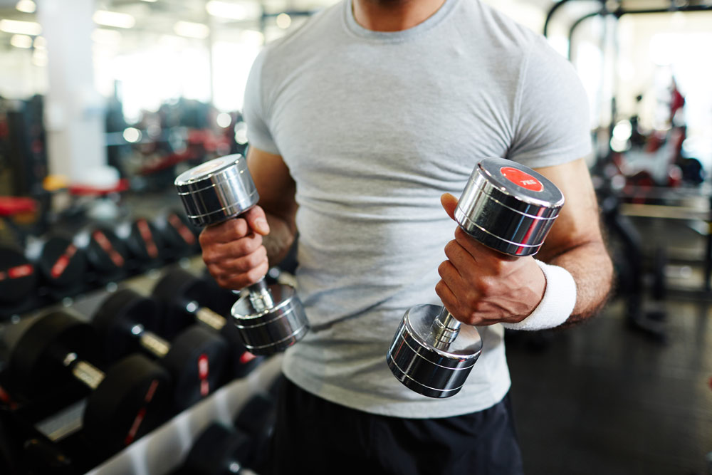 A man at the gym holding two dumbbells getting ready to work out.