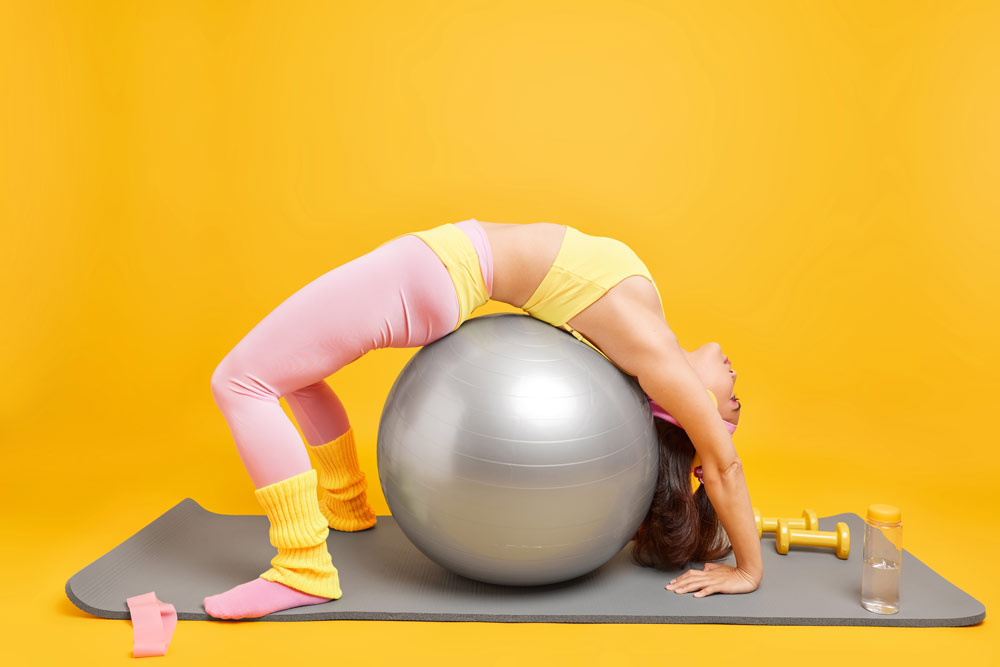 A woman stretching over an exercise ball on top of an exercise mat.