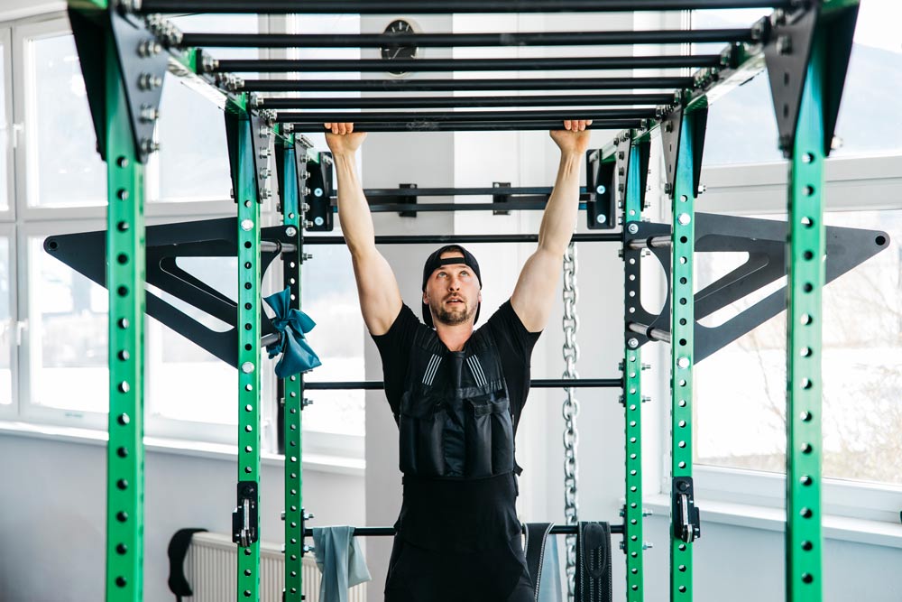 A man in a black hat is in a metal cage doing pull-ups